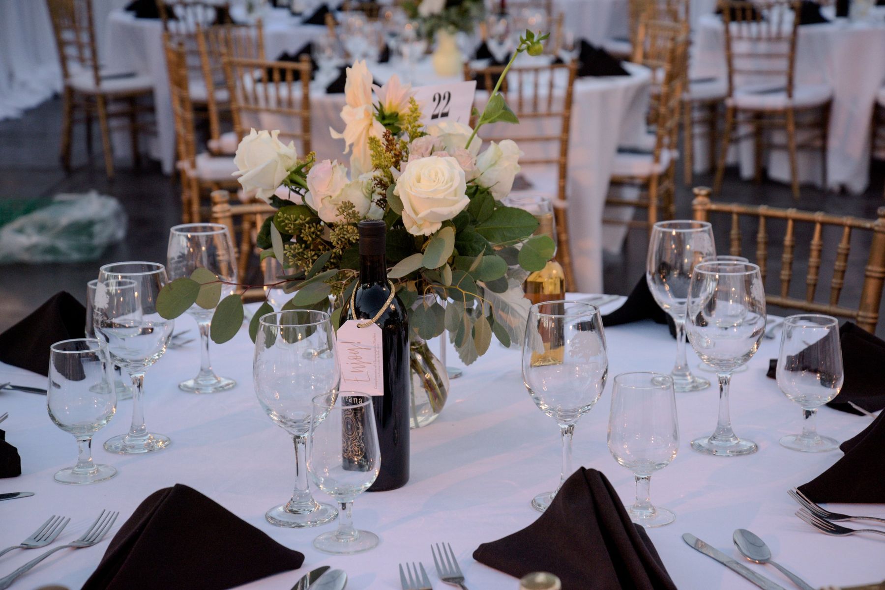 Moncus Park Evening Under the Oaks event: round reception table set with white roses, a wine bottle, and gold chairs