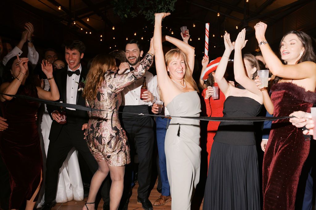 Moncus Park Christmas wedding: guests cheering and dancing at the reception under string lights
