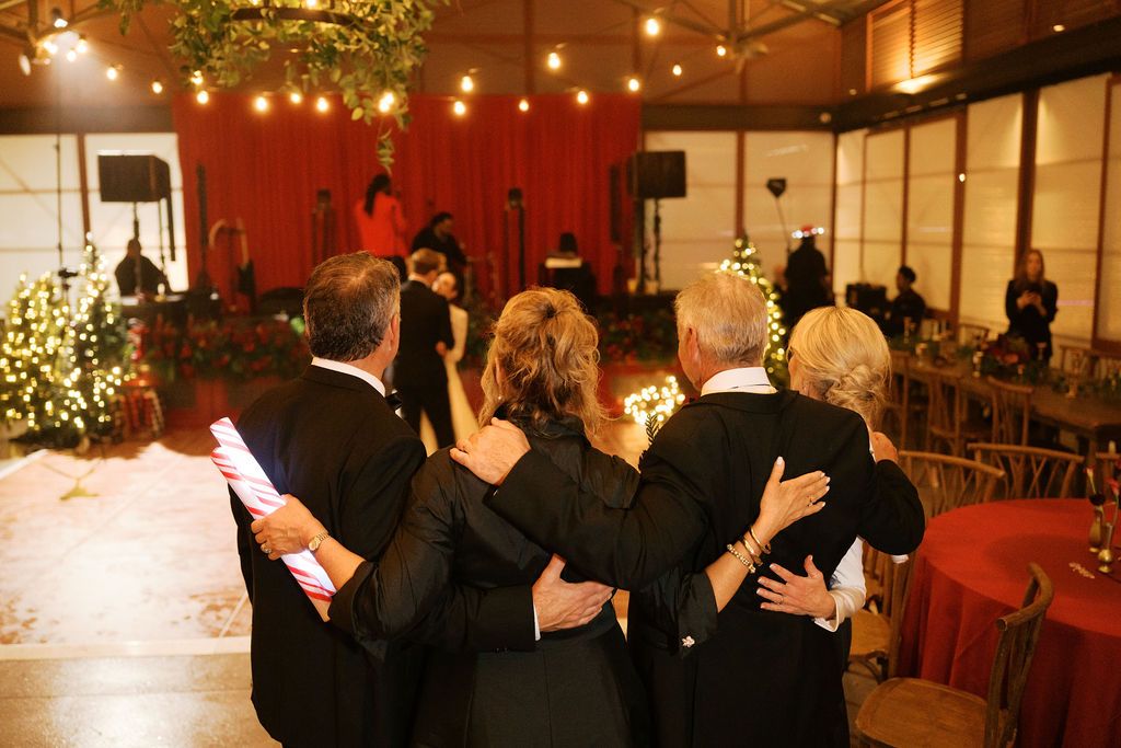 Moncus Park Christmas wedding: loved ones watching the first dance, with lit Christmas trees and a red-curtained stage