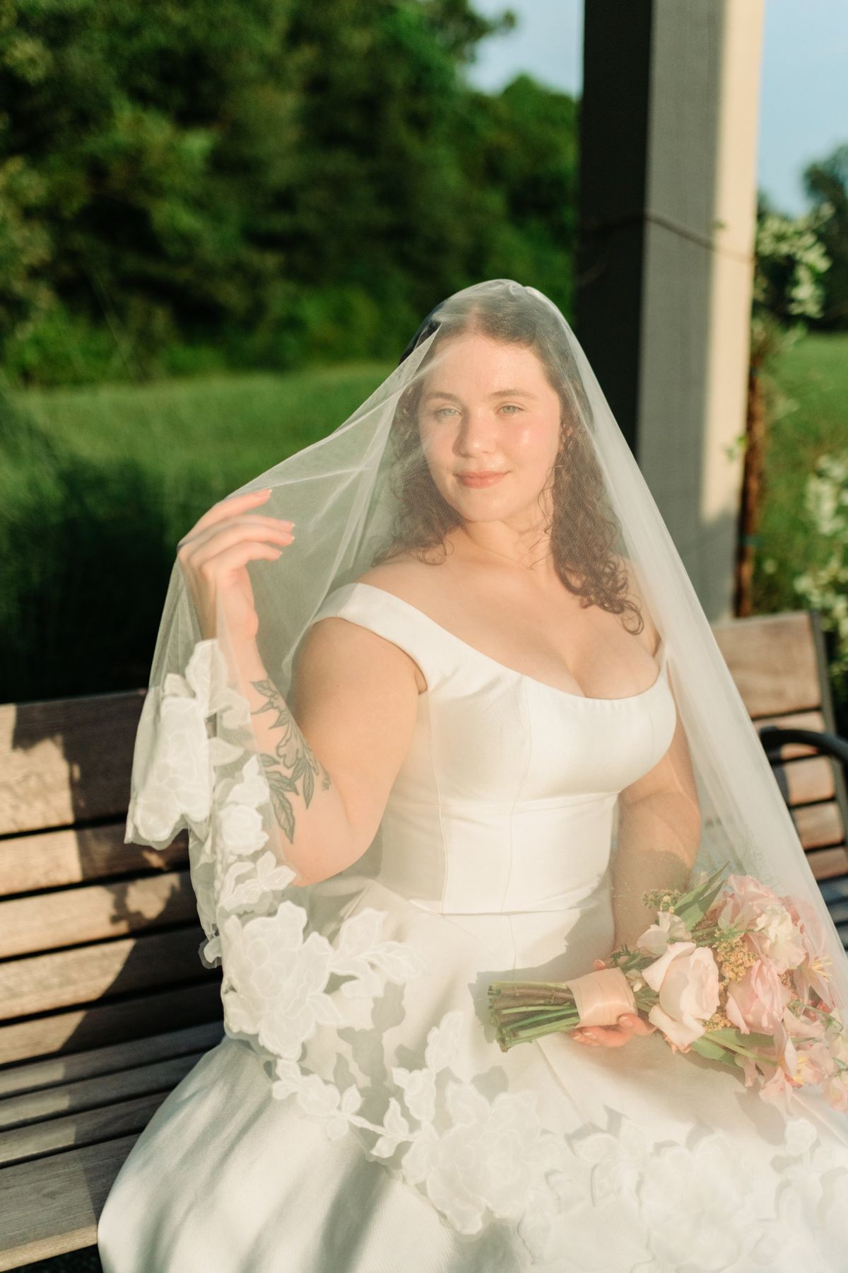 Moncus Park: bride in a lace-trimmed veil sitting on a bench in golden evening light, holding a pink bouquet