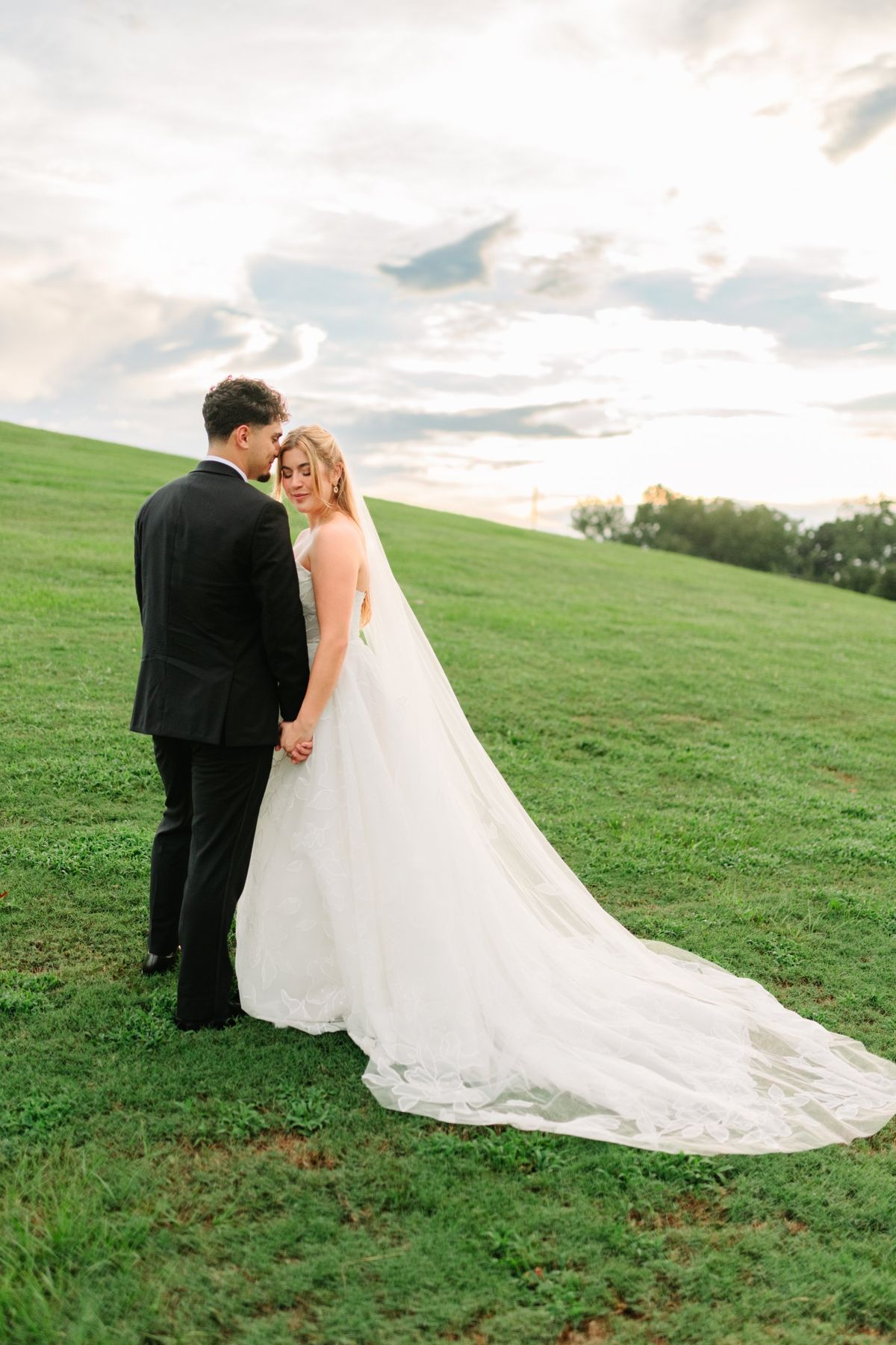 Moncus Park: couple embracing on a grassy hill at sunset with the bride's long veil trailing behind