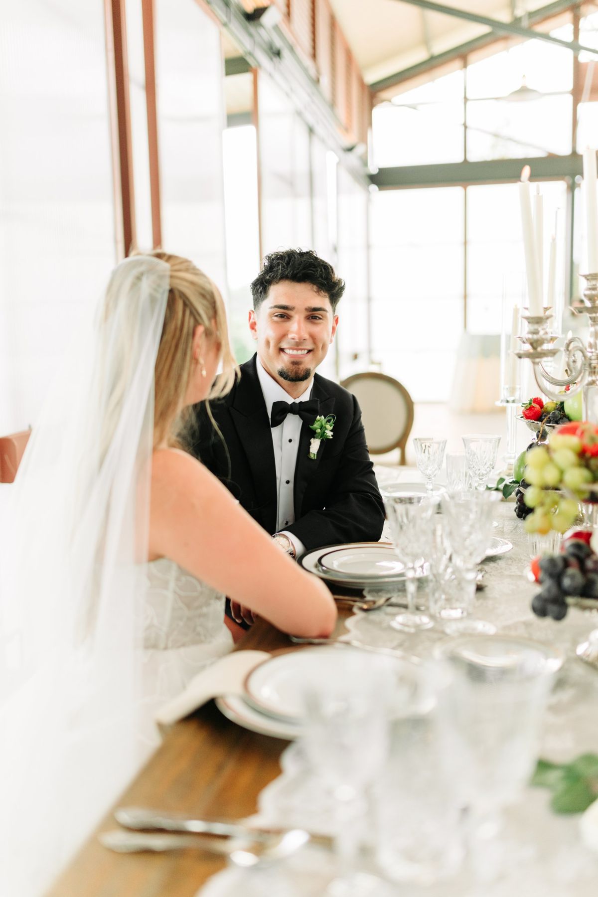 Moncus Park: groom smiling at the sweetheart table in the Doerle Pavilion with the bride in her veil beside him