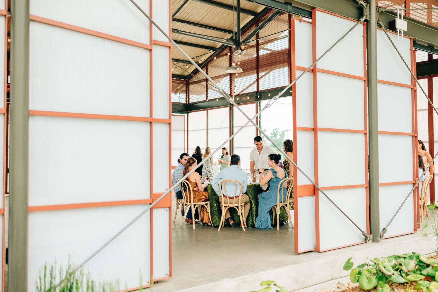 Moncus Park: guests seated at a round table with green velvet linen, seen through the Doerle Pavilion panels